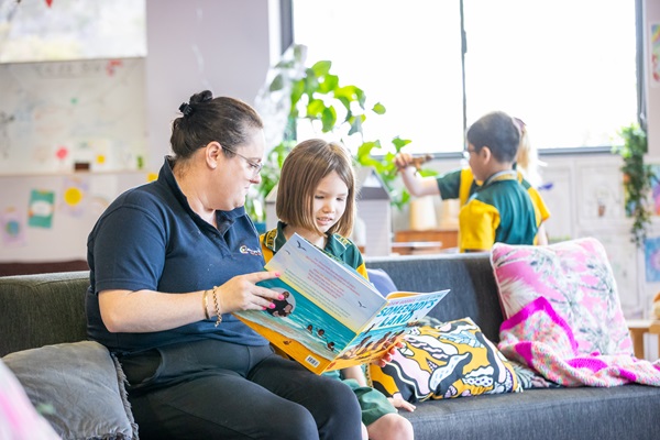 Outside school care educator reading with a student in a relaxed indoor space, highlighting care, wellbeing and engagement beyond regular school hours