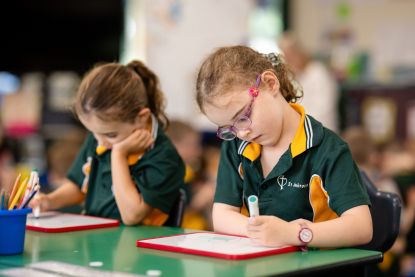 Students in school uniform working independently at their desks, highlighting early learning, concentration and classroom engagement at St Ambrose’s Primary School