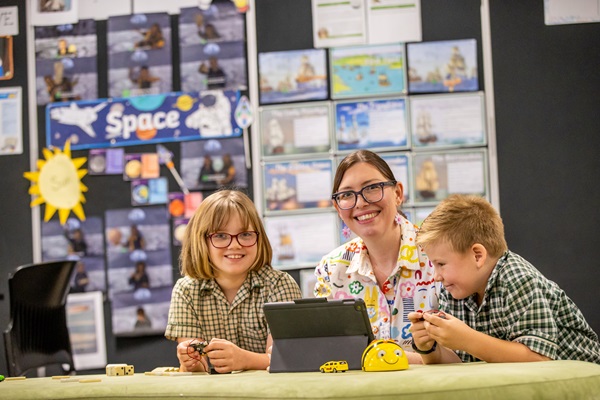 Students and a teacher collaborating around a tablet during a classroom learning activity, highlighting guided learning, digital engagement and supportive teaching at St Ambrose’s Primary School