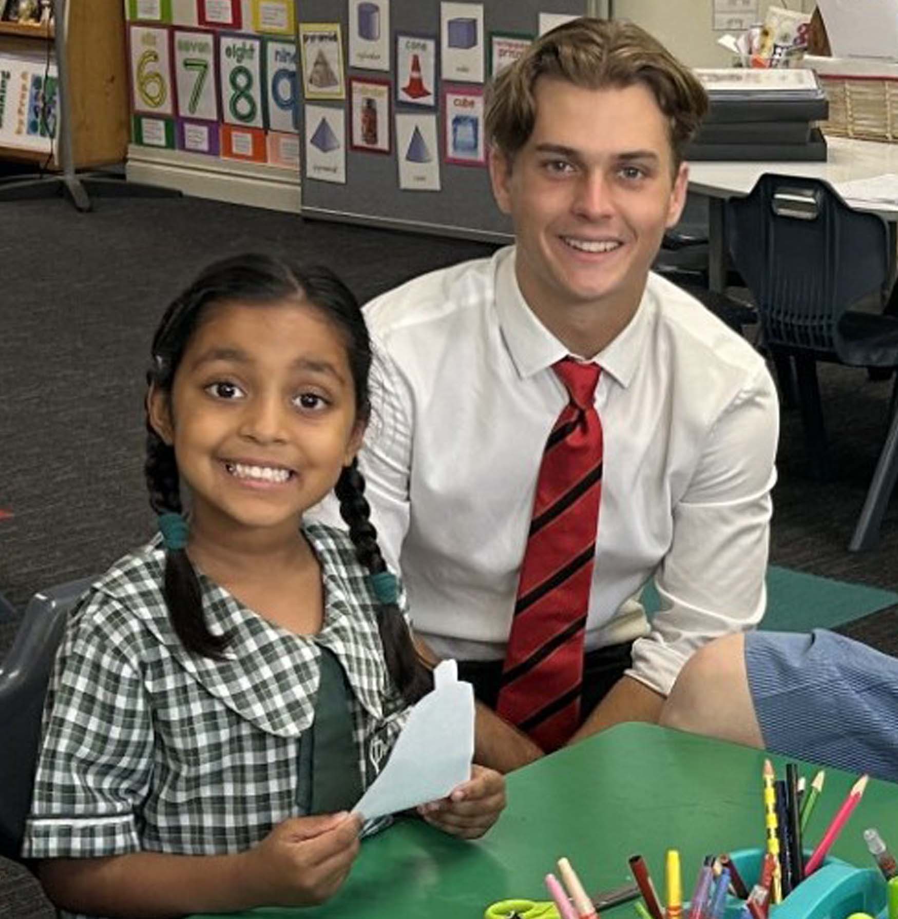 Older student supporting a younger student during a classroom learning activity, reflecting positive role modelling and supportive learning relationships